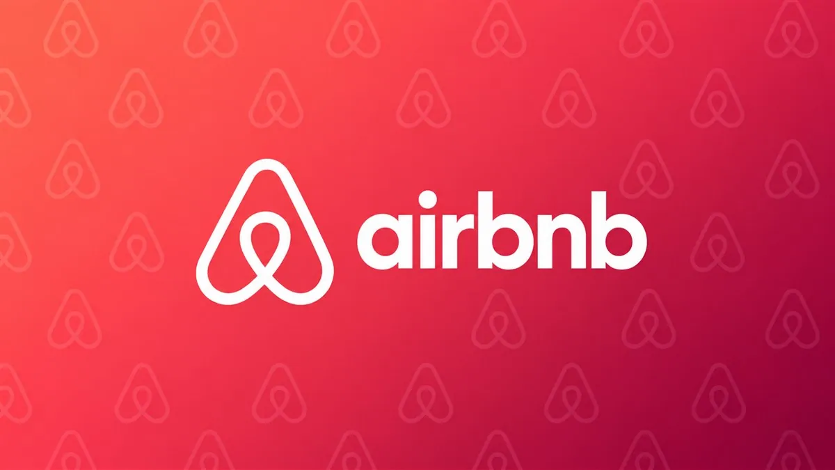 Logomarca branca do Airbnb sobre fundo coral com padrão diagonal
